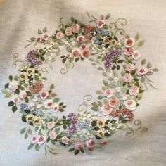 an embroidered wreath with pink and blue flowers on white linen, surrounded by green leaves