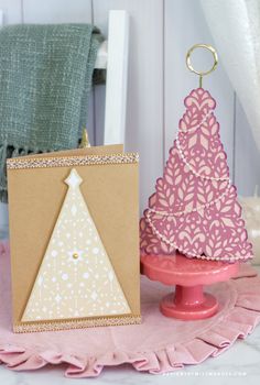 two small christmas trees are sitting on a pink plate next to a brown card holder