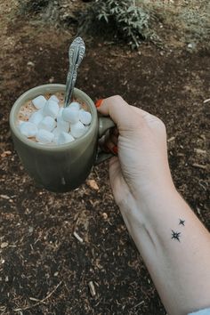 a person holding a mug with marshmallows in it and a spoon sticking out of the cup