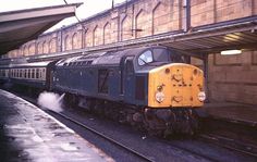 a yellow and black train traveling down tracks next to a building