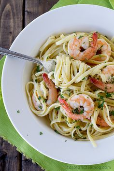 a white bowl filled with pasta and shrimp on top of a green napkin next to a fork