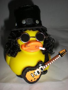 a yellow rubber duck with glasses and a hat, holding a guitar in its mouth