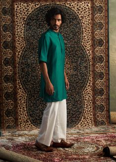 This short sleeved kurta is a stylish standout, showcasing distinctive embroidery on the placket with a unique half-half motif that truly sets it apart. When paired with loose pyjamas, the ensemble effortlessly combines traditional charm with modern flair, all while remaining minimalistic and comfortable. It’s the ideal choice for those looking to make a fashionable statement and celebrate a blend of classic and contemporary style. Men Kurta, Green Shorts, Mandarin Collar, Aza Fashion, Half Sleeves, Emerald Green, Contemporary Style, Emerald, Embroidery