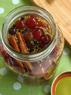 a glass jar filled with fruit and spices on top of a green table cloth next to a wooden cutting board