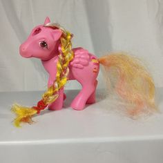 a pink toy pony with yellow mane and braid on its tail sitting on a white surface