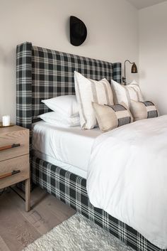 a bed with white sheets and black plaid headboard next to a night stand in a bedroom