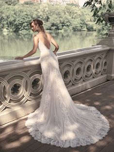 a woman in a wedding dress standing on a bridge looking at the water and trees