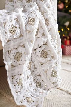 a white crocheted blanket sitting on top of a couch next to a christmas tree