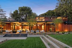 a modern house is lit up at night with lights on the patio and lawn area