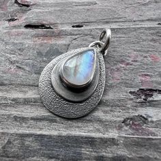 This Rainbow Moonstone teardrop pendant is handmade from a natural Rainbow Moonstone cabochon and sterling silver.  The smooth cabochon has been set in two layers of sterling silver.  I have made this pendant by sawing, soldering, texturing, and finishing the design entirely by hand.  The silver has been oxidized and polished to create an antique patina finish. This pendant does not include a chain.  If you would like to order a chain like the one modeled with the pendant, you can find this chain as well as more chain styles and lengths in the 'Chains' section of my shop.  Be sure to see all photos and video for size and color reference. Select your choice of stone when ordering. Pendant Size (Not Including Bail): About 19x24mm Rainbow Moonstone: About 10x13mm Wise Handmade Jewelry is an e Hand Forged Teardrop Moonstone Jewelry, Artisan Teardrop Moonstone Jewelry, Silver Moonstone Teardrop Pendant Jewelry, Silver Moonstone Round Pendant Jewelry, Silver Moonstone Teardrop Pendant, Bohemian Moonstone Round Pendant Jewelry, Rainbow Moonstone Pendant, Rainbow Moonstone, Fine Silver