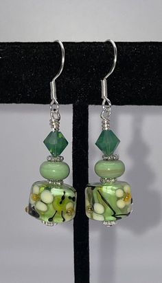 "I designed and created these earrings using artisan lampwork barrel beads.  They are so pretty and bright!  Mint green barrel beads with white flowers and black vines.  I paired them with artisan donut spacer beads in a beautiful almost sage green.  I used bright silver daisy spacers and finished them off with palace green opal Swarovski crystals.  They are securely wire wrapped and suspended from sterling silver ear wires.  Earrings measure approximately 1.75\" long  Will come gift boxed" Handmade Green Flower Bead Earrings, Green Flower Earrings With Round Beads, Green Flower Earrings With Dangling Beads, Unique Green Earrings With Colorful Beads, Green Dangle Earrings With Colorful Beads, Unique Green Czech Glass Beaded Earrings, Green Czech Glass Flower Earrings, Green Flower-shaped Jewelry With Dangling Beads, Easy Jewelry