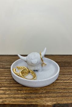 a small white bird on a plate with two gold rings in it's mouth