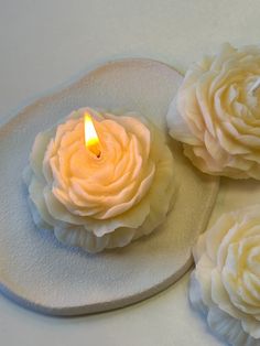 three white flowers sitting on top of a plate with a lit candle in the middle