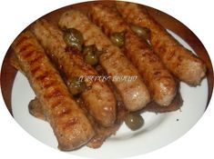 several sausages on a white plate with olives