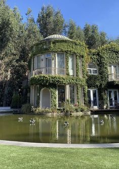 a woman is standing in front of a house with birds flying around the pond and trees behind her