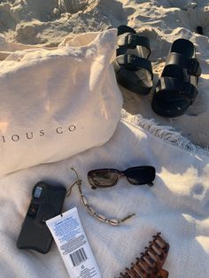 some items are laying out on a towel near the sand and water, including sunglasses, an object that says house co