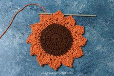 an orange and brown crochet doily on blue surface with yarn in the middle