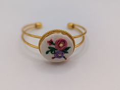 This beautiful electroplated copper bracelet is delicately adorned with a stunning embroidered floral centerpiece, making it the perfect accessory to add a touch of elegance and charm to any outfit. The bracelet is adjustable, allowing for a comfortable and secure fit on any wrist size. The copper plating gives it a luxurious shine. The floral embroidery is handcrafted with care, showcasing intricate details and vibrant colors. Its unique design is sure to make a statement and elevate any look. Bohemian Embroidered Cuff Bracelet As Gift, Bohemian Embroidered Cuff Bracelet For Gift, Spring Gift Cuff Bracelet, Spring Gift Adjustable Cuff Bracelet, Adjustable Spring Cuff Bracelet As Gift, Adjustable Spring Cuff Bracelet Gift, Adjustable Flower Cuff Bracelet For Spring, Elegant Adjustable Decorative Bracelets, Elegant Embroidered Bracelets As Gift