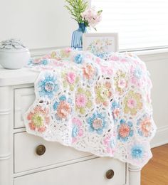 a crocheted blanket on a dresser with flowers