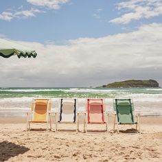 four lawn chairs sitting on top of a sandy beach next to the ocean under an umbrella