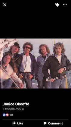 four men are standing on the deck of a sailboat, posing for a photo