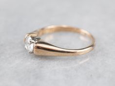 a gold ring with a white diamond on the top, sitting on a gray surface