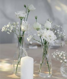 three vases filled with white flowers on top of a table next to a candle