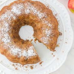 an apple cider bundt cake on a white plate with powdered sugar and apples in the background