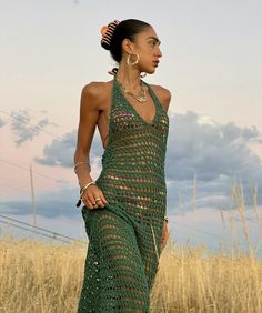 a woman in a green crocheted dress standing in a field with tall grass