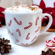 a white cup filled with hot chocolate on top of a table next to candy canes