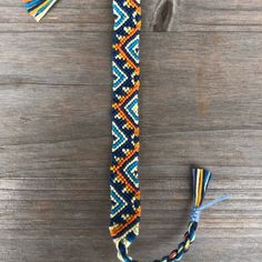 a blue, yellow and white beaded cross with tassels sitting on a wooden surface