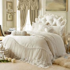 a white bed sitting in a bedroom next to a window covered in curtains and pillows