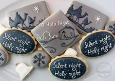 decorated cookies on a white plate with words written in black and white, including an image of a nativity scene