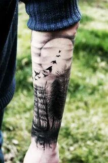 a person with a tattoo on their leg that has trees and birds flying over them