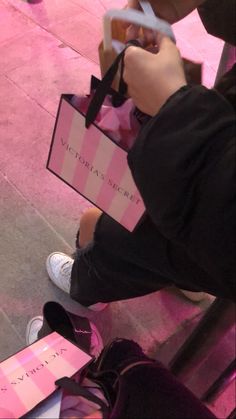 a person sitting on the ground holding a pink and white bag with a black ribbon