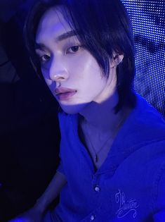 a young man with black hair and blue shirt sitting in front of a computer screen