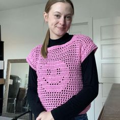 a woman standing in front of a mirror wearing a pink crocheted sweater and jeans