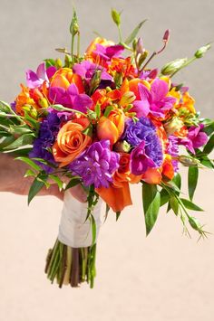 a bridal bouquet with orange, purple and pink flowers in the palm of someone's hand