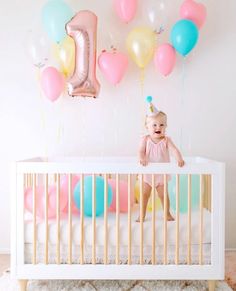 a baby sitting in a crib with balloons