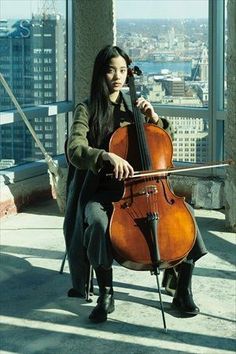 a woman sitting on top of a building holding a cello