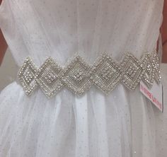 a white dress with silver beading on it and a ribbon around the waistline