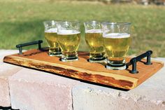 four glasses of beer are sitting on a wooden tray