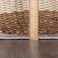 a wooden ruler sitting on top of a floor next to a woven basket with a measuring tape