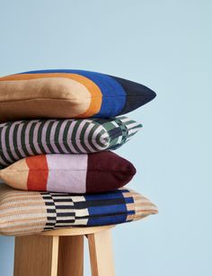 four pillows stacked on top of each other in different colors and patterns, sitting on a stool