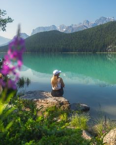 a woman sitting on top of a rock next to a lake