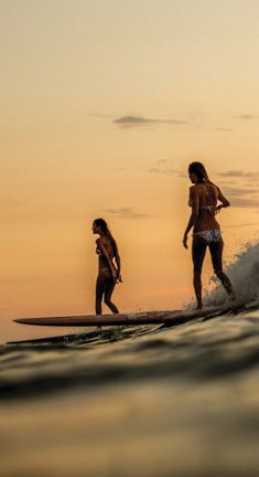 two people on surfboards in the ocean at sunset