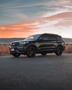 the black suv is parked on the side of the road in front of an orange sunset