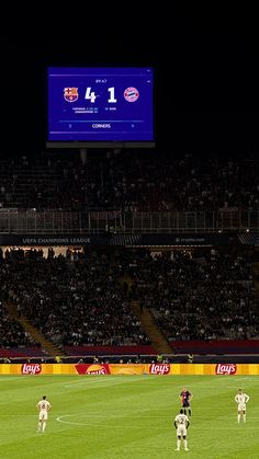 soccer players are on the field in front of a large scoreboard at night time