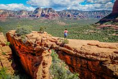 a man standing on the edge of a cliff looking out over a valley and mountains