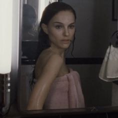 a woman in a bathrobe looking at herself in the mirror